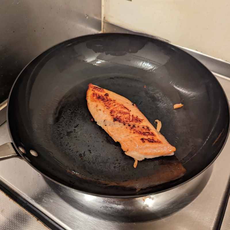 キッチンのひとくちコンロでリバーライト極フライパンを使って鮭を焼いた画像。フライパンの中央に鮭の切身が一匹こんがりと焼けている。